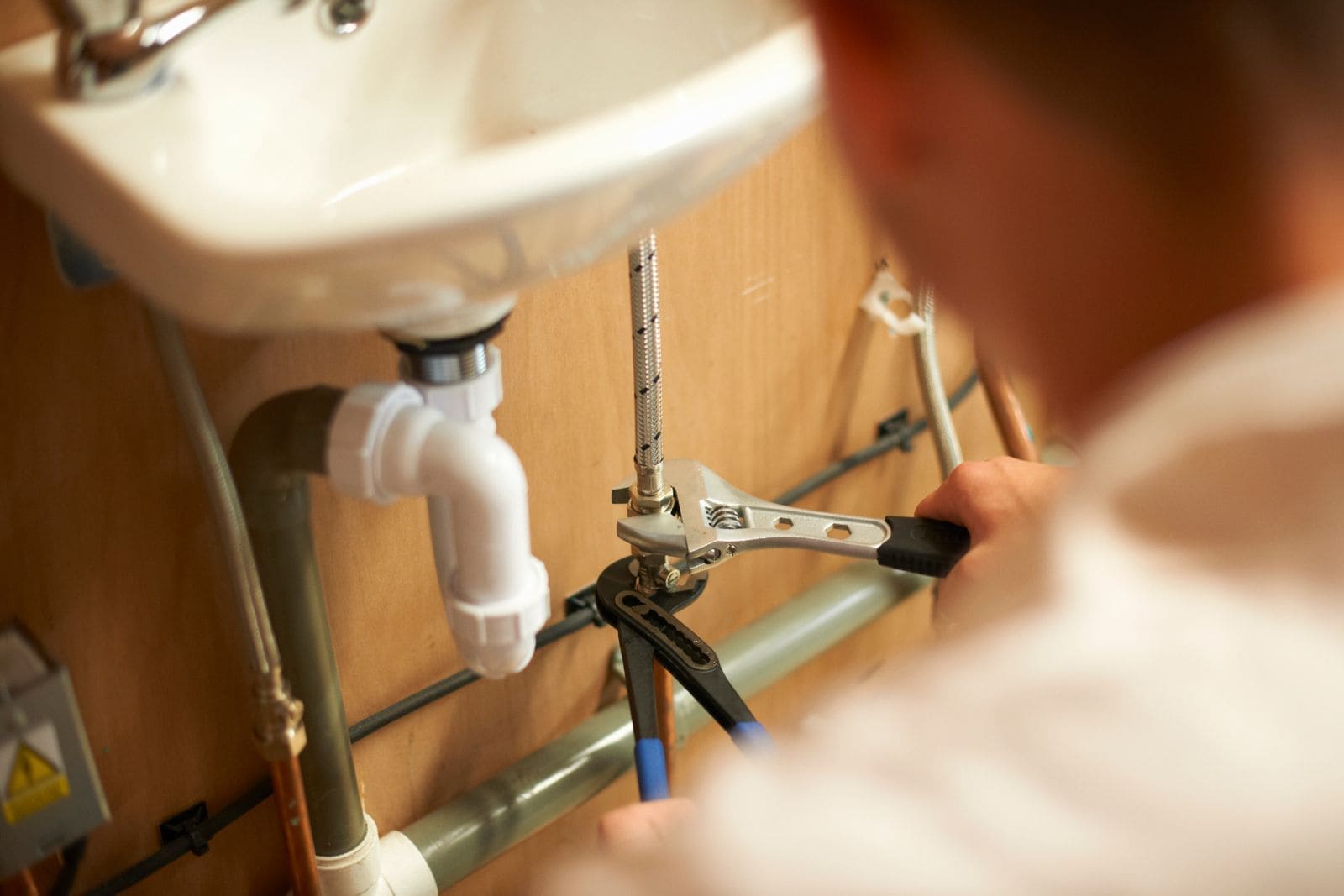 Fontanero montando el sifón y los latiguillos bajo un lavabo durante una reforma