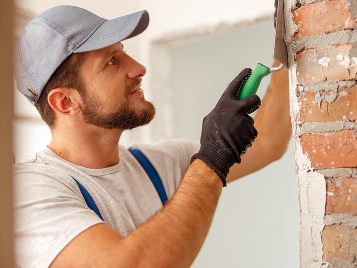 Albañil con guantes preparando con la espátula una pared junto al ladrillo visto