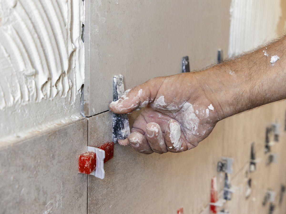 Operario colocando azulejo con crucetas niveladoras sobre cemento cola en la pared de un baño