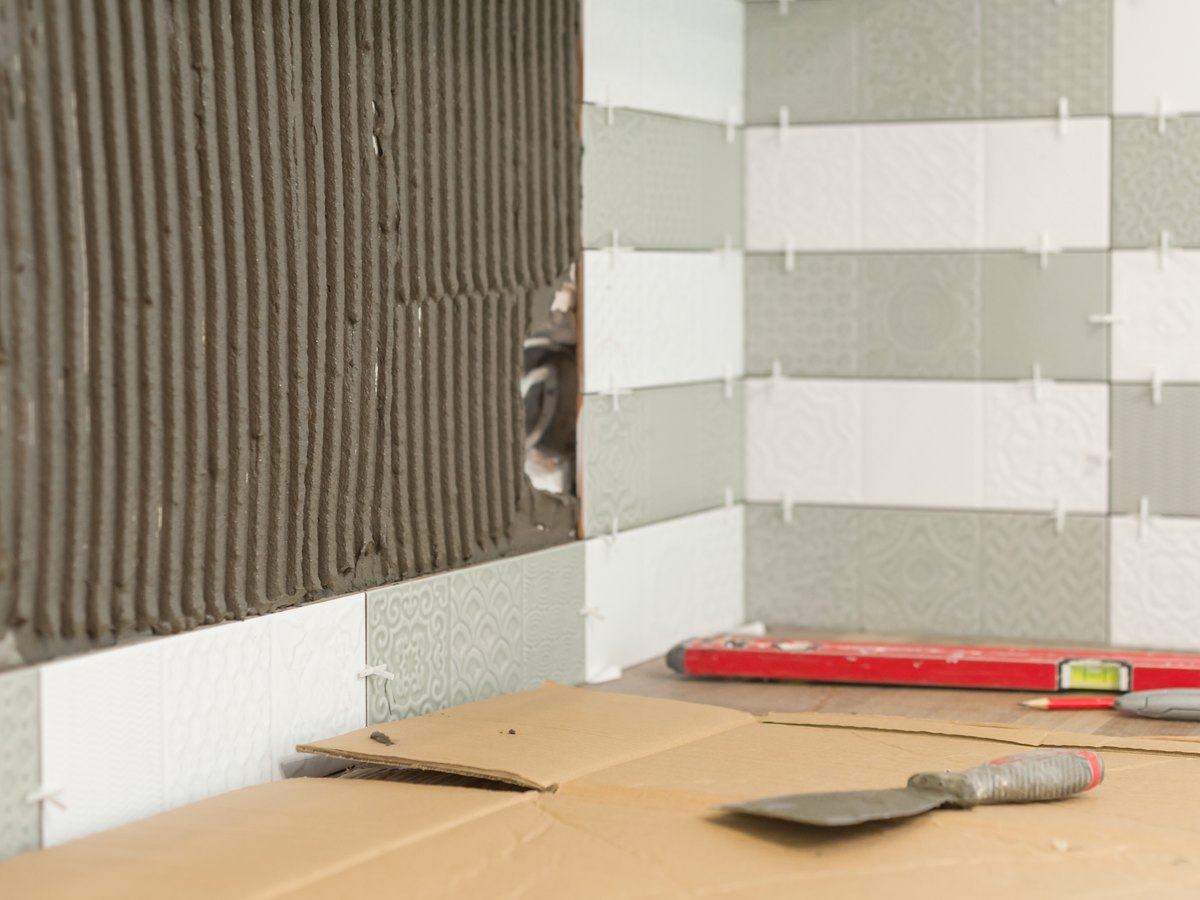 Pared de un baño a medio alicatar, con cemento cola peinado, crucetas y nivel