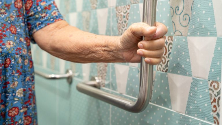 Persona mayor sujetándose a la barra de apoyo de un baño adaptado, la obra que cubre la ayuda municipal de accesibilidad