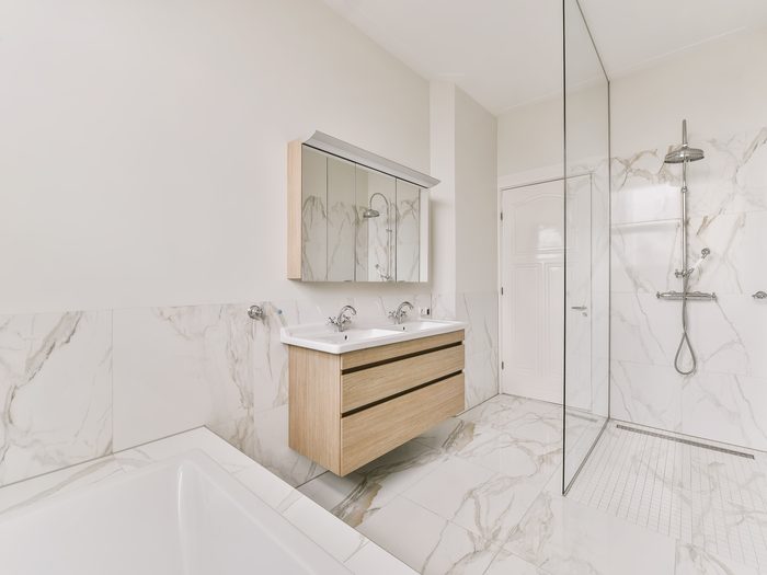 Baño con porcelánico imitación mármol de gran formato en la pared y ducha con mampara fija
