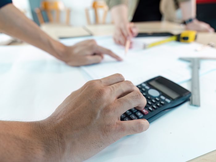 Mano tecleando en la calculadora el presupuesto de una obra sobre los papeles del proyecto