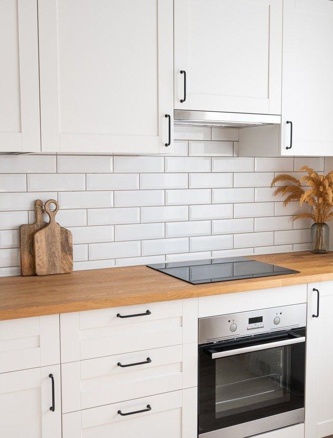 Cocina con azulejo blanco tipo metro, encimera de madera y horno integrado