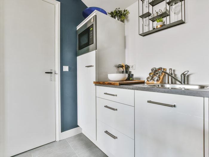 Cocina pequeña y funcional con muebles blancos, microondas en columna y fregadero de acero