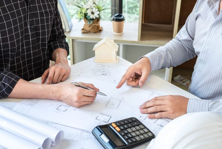 Dos personas revisando los planos de una reforma sobre la mesa, con calculadora y maqueta de vivienda