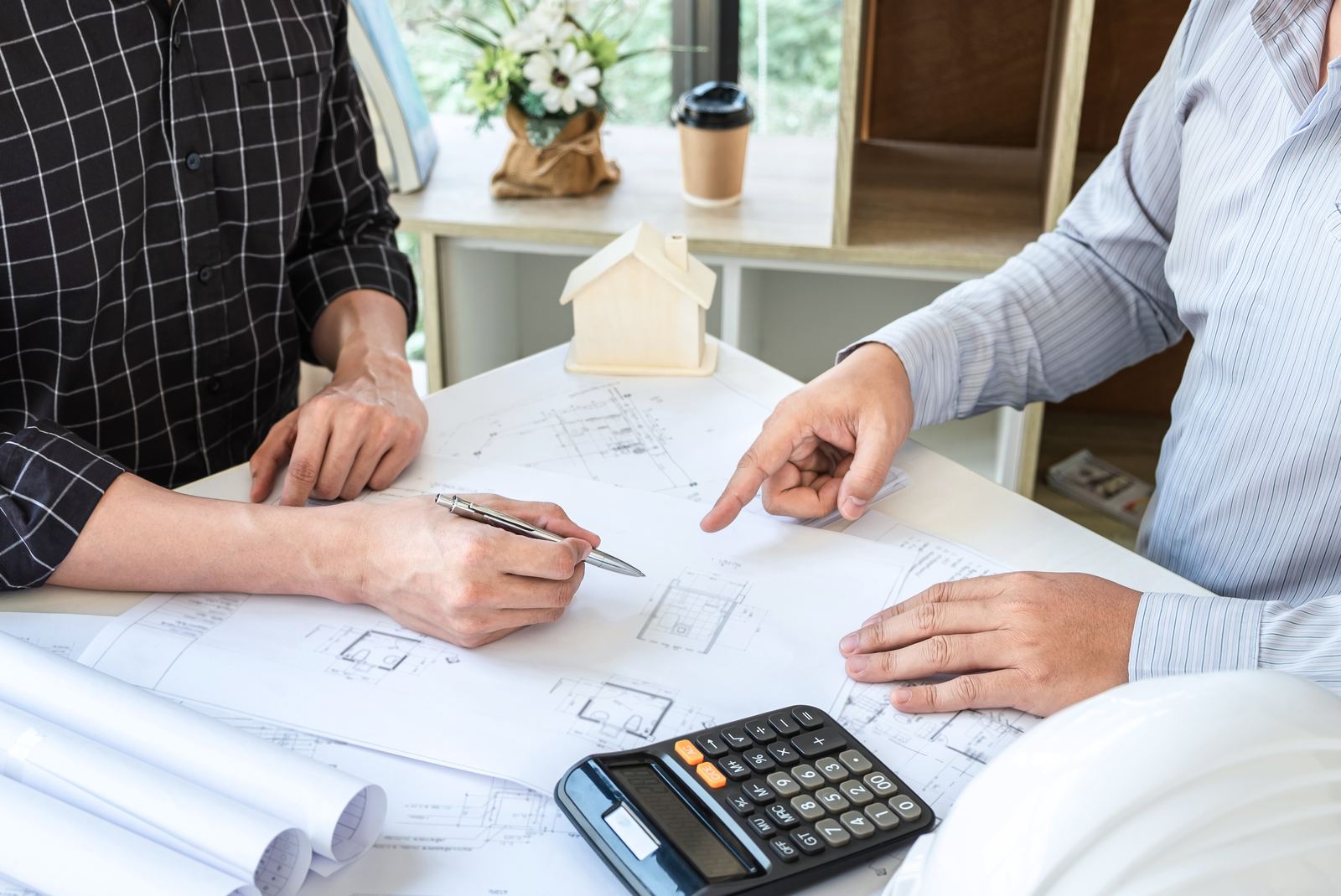 Dos personas revisando los planos de una reforma sobre la mesa, con calculadora y maqueta de vivienda