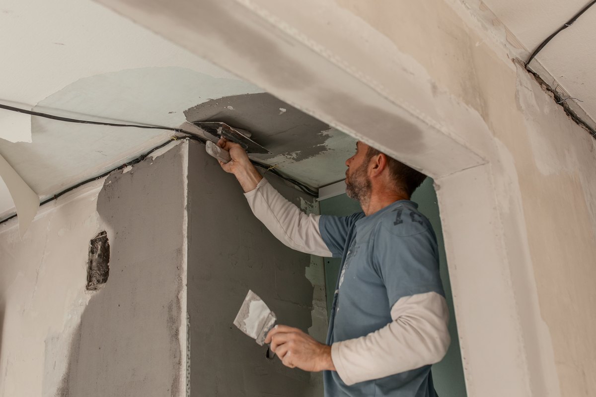 Operario saneando con llana el encuentro de pared y techo de una vivienda en obra