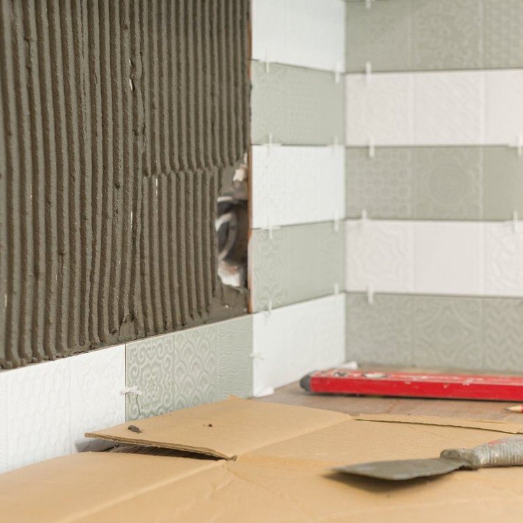 Pared del baño a medio alicatar, con el cemento cola peinado y las herramientas en el suelo