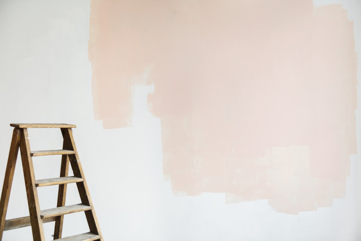 Pared lisa ya saneada con la primera mano de pintura a medio dar y una escalera de madera