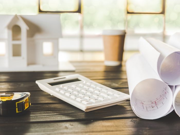 Planos enrollados, calculadora y flexómetro sobre la mesa para preparar el presupuesto de un local