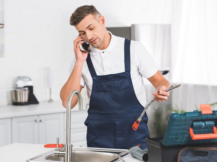Operario con peto de trabajo hablando por teléfono junto al fregadero de una cocina