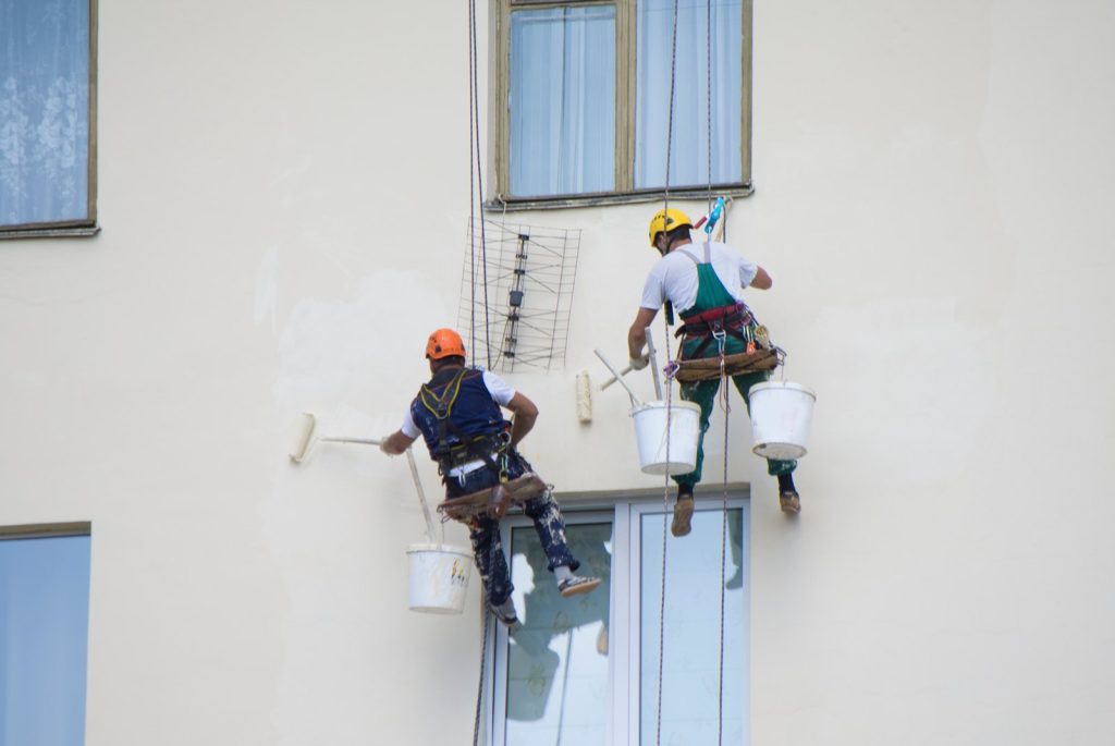 Dos pintores con arnés pintando la fachada de un bloque de viviendas en Zaragoza
