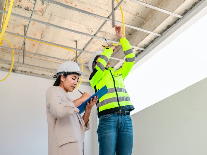 Técnica con casco tomando notas mientras un operario con chaleco reflectante revisa la estructura del falso techo de la obra