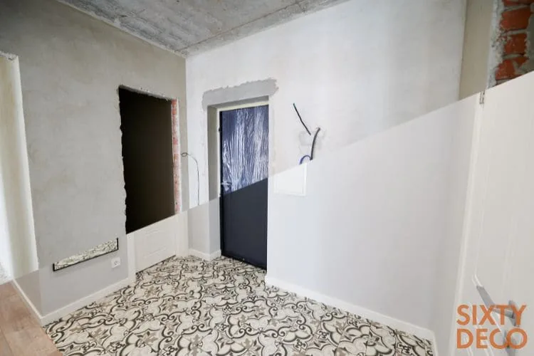Recibidor partido en dos: hueco de puerta en obra junto al acabado con puerta negra y suelo hidráulico, albañilería construcción Zaragoza