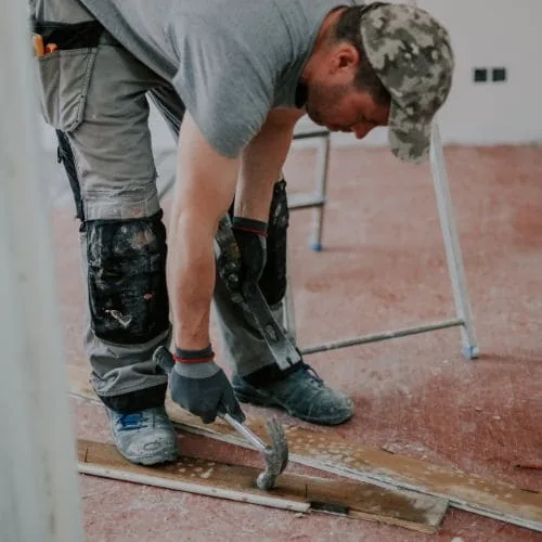 Albañil con gorra y rodilleras clavando listones en el suelo de una obra, albañilería de calidad Zaragoza