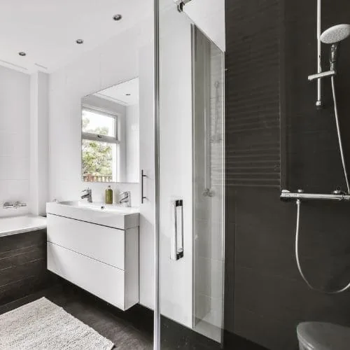 Baño reformado con mampara de cristal, ducha de columna y mueble de lavabo blanco junto a la ventana, baños modernos Zaragoza