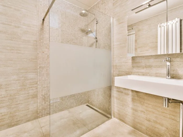 Ducha a ras de suelo con sumidero lineal, mampara de vidrio y pared de mosaico beige, cambiar bañera por plato de ducha precio Zaragoza