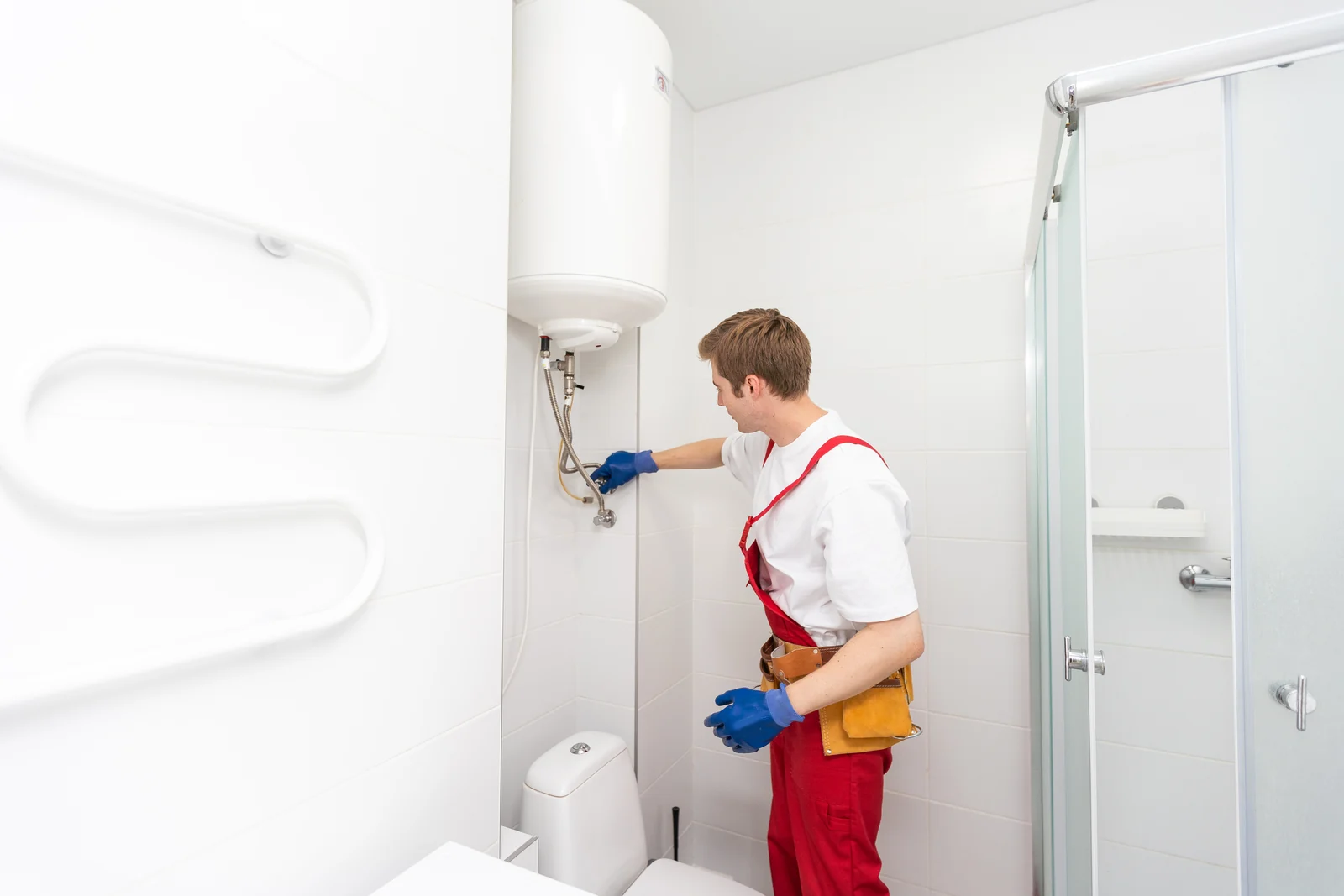 Fontanero con mono rojo conectando los latiguillos de un termo eléctrico colgado en la pared del baño, cambiar termo eléctrico precio Zaragoza