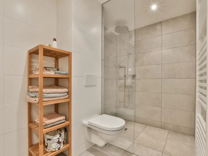 Baño pequeño con ducha a ras de suelo, mampara fija de vidrio, inodoro suspendido y estantería de madera, cambio bañera por ducha precio Zaragoza