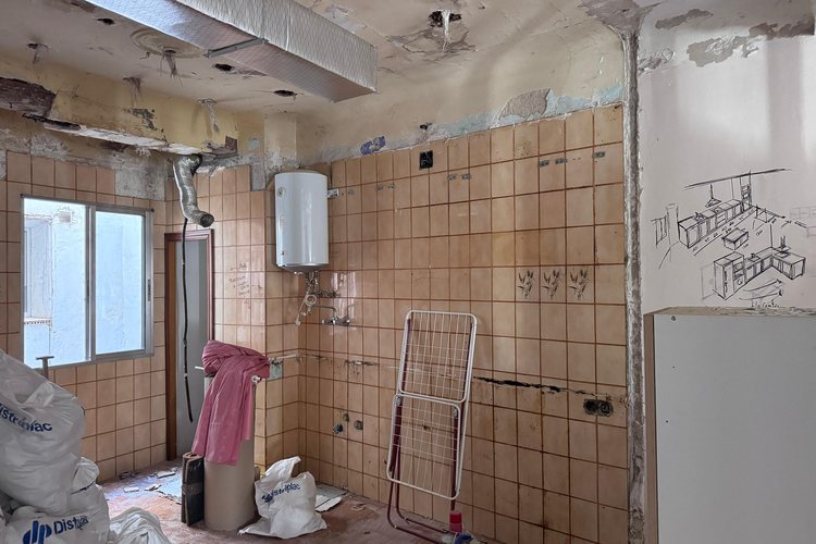 Cocina antes de la reforma, con el alicatado antiguo, el termo a la vista y los escombros en el suelo