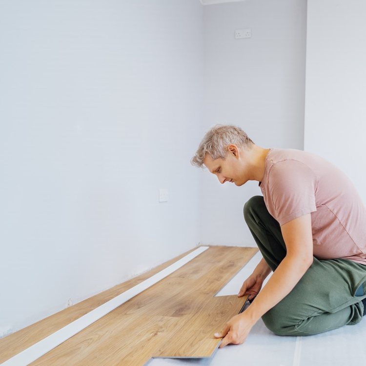 Operario colocando suelo laminado de madera clara en una habitación vacía