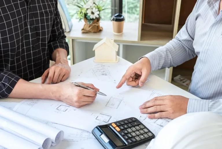 Dos personas revisando los planos de una reforma sobre la mesa, con calculadora y una maqueta de casa, cómo elegir empresa de reformas Zaragoza
