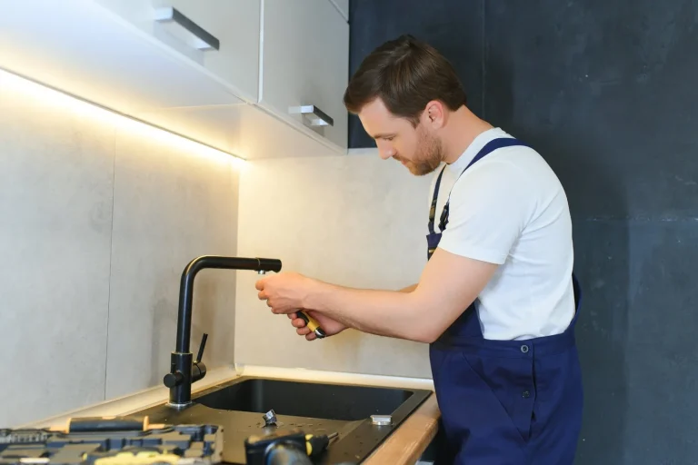 Fontanero con peto azul ajustando el grifo negro de un fregadero de cocina, cuánto cobra un fontanero Zaragoza