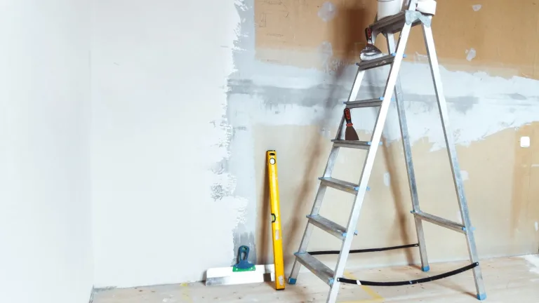 Escalera de tijera, nivel y espátula junto a una pared a medio enlucir, cuánto cuesta una reforma barata Zaragoza