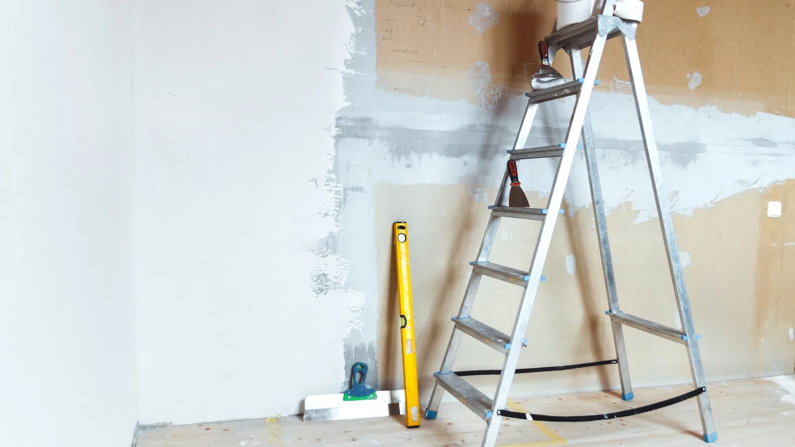Escalera de tijera, nivel y espátula junto a una pared a medio enlucir, cuánto cuesta una reforma barata Zaragoza