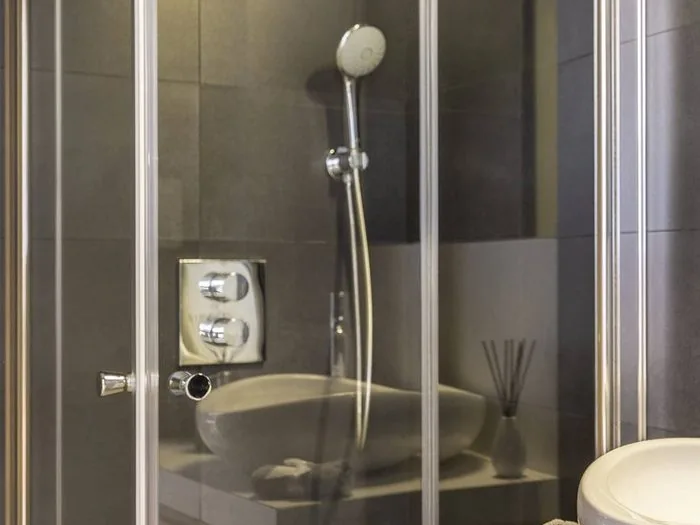 Ducha con mampara plegable de vidrio, grifo termostático y azulejo gris oscuro, diseño de baños pequeños Zaragoza
