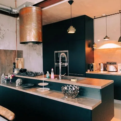 Cocina con isla verde oscuro, campana de cobre y lámparas colgantes, diseño de cocinas Zaragoza
