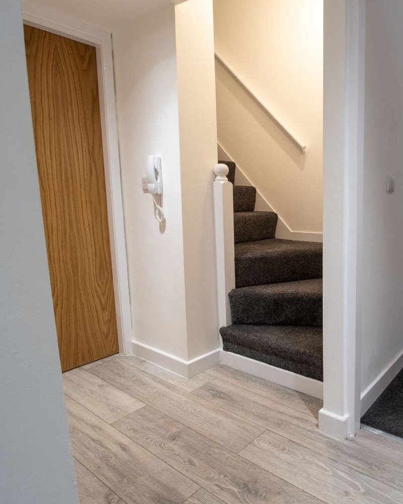 Entrada de vivienda reformada con escalera, suelo laminado y puerta de madera