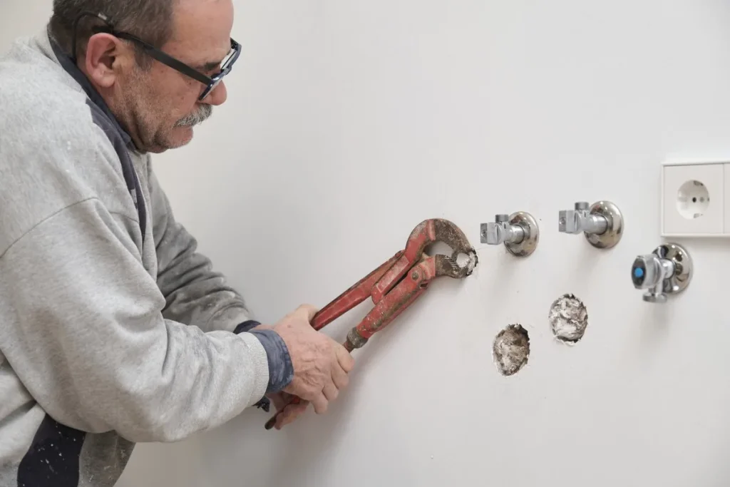 Fontanero apretando con una llave de grifa las llaves de paso nuevas de una pared, instalación fontanería reformas Zaragoza