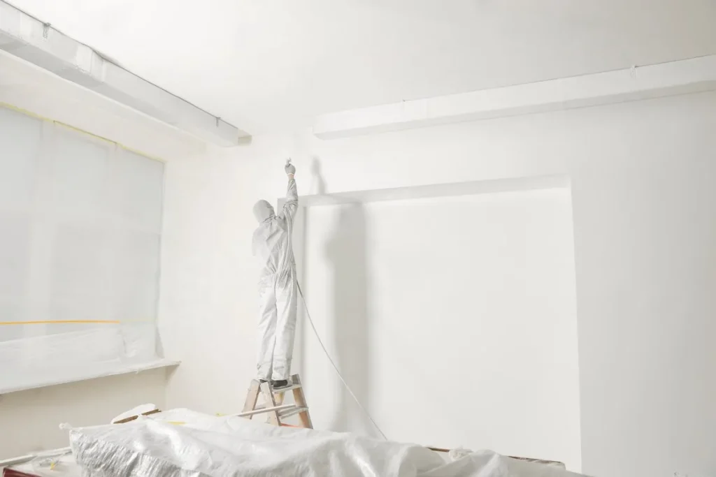 Pintor con mono protector pintando con pistola las paredes de una habitación vacía, mejores empresas de tratamiento de humedades en Zaragoza