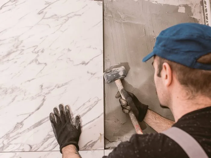 Operario colocando una pieza grande de porcelánico imitación mármol con la maza de goma, precio cambiar bañera por plato de ducha Zaragoza