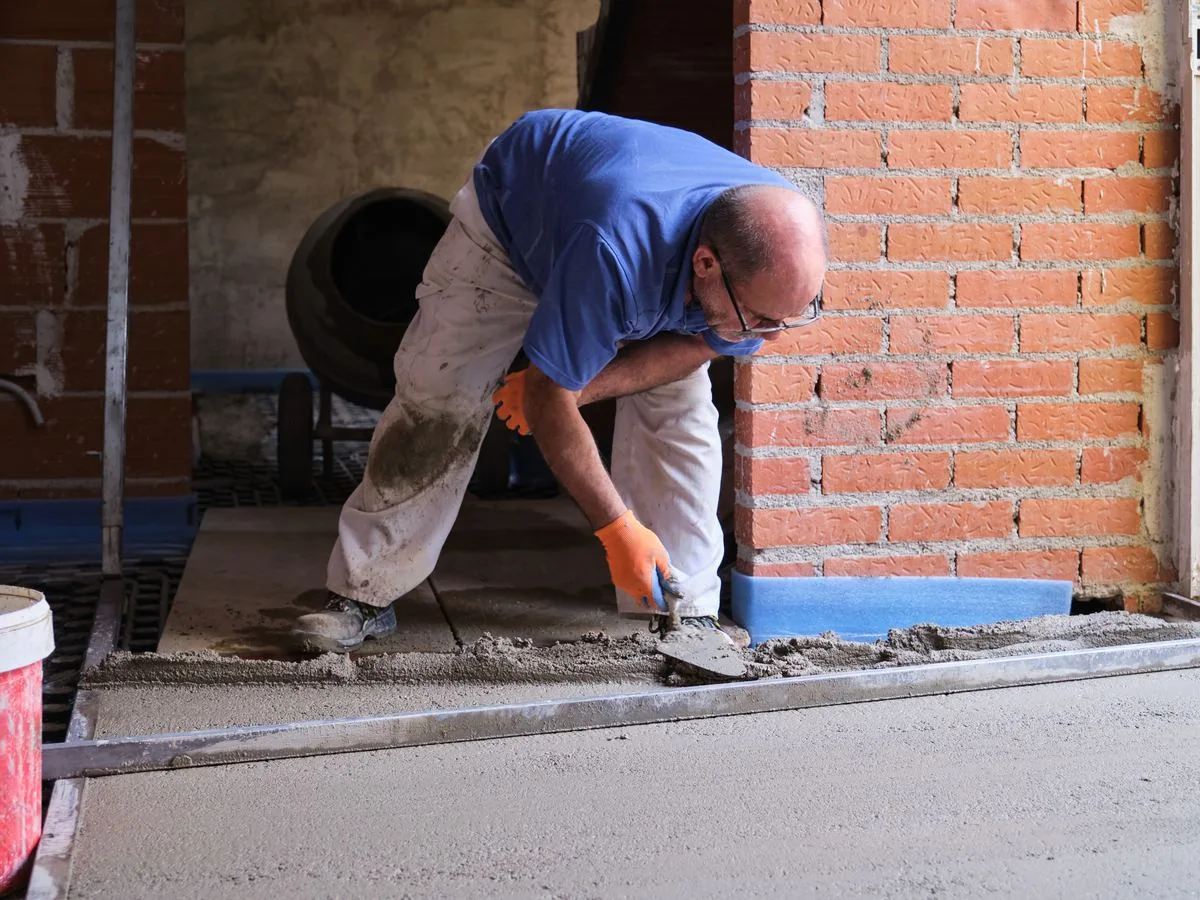 Albañil extendiendo mortero con maestras para nivelar el suelo junto a una pared de ladrillo, precio de mano de obra de alicatado Zaragoza