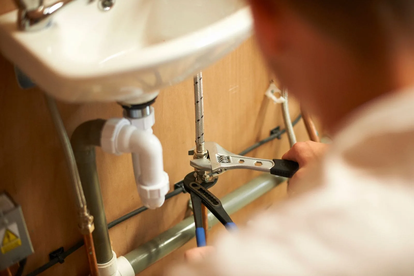 Fontanero apretando con una llave inglesa la tubería bajo un lavabo, precio fontanero hora Zaragoza