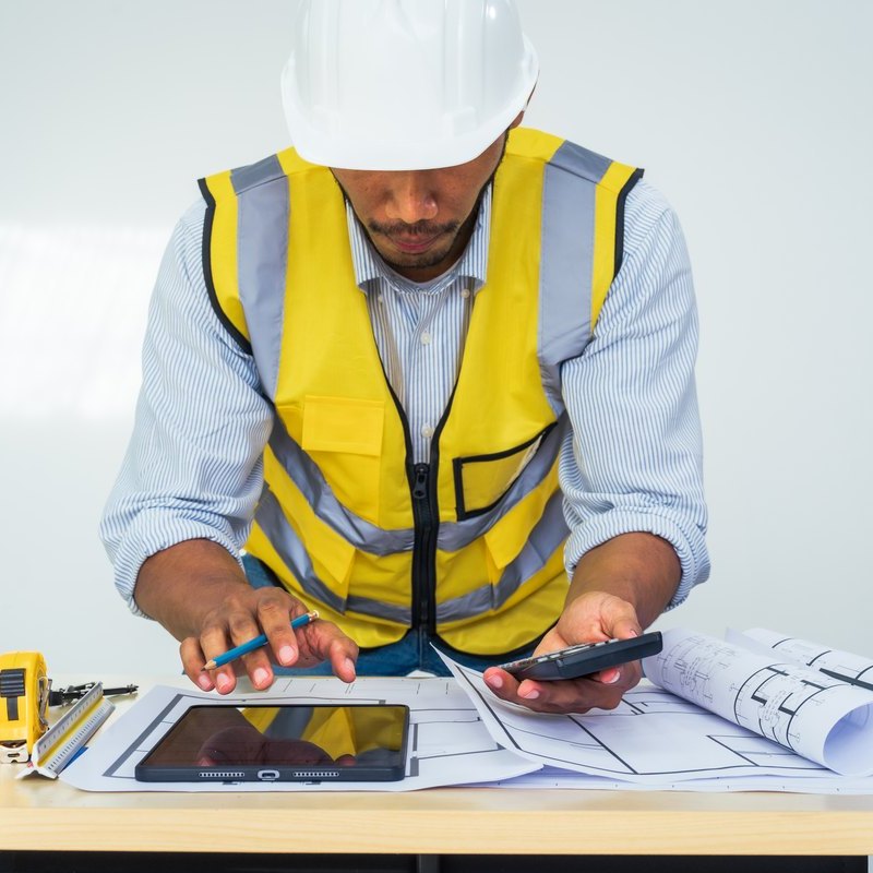 Técnico con casco y chaleco calculando el presupuesto sobre los planos de la obra, presupuesto reforma local comercial Zaragoza