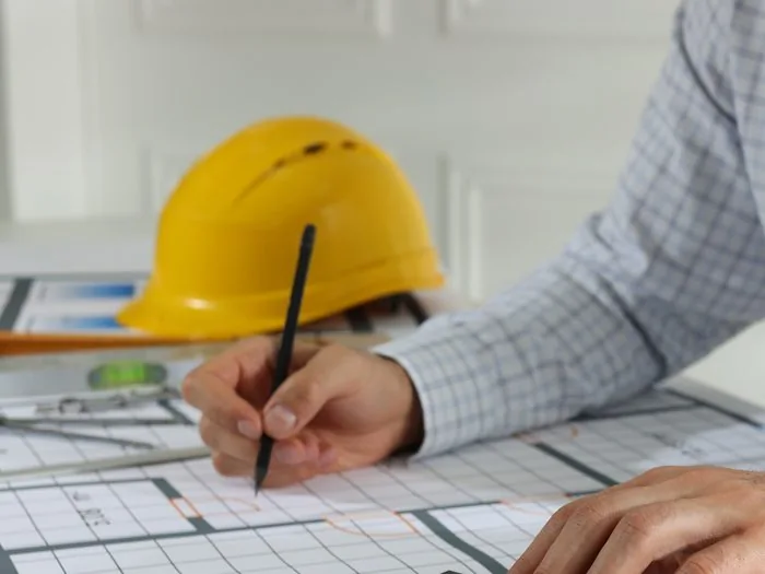 Técnico marcando con lápiz los planos de una reforma, con el casco de obra sobre la mesa, presupuesto reforma vivienda Zaragoza