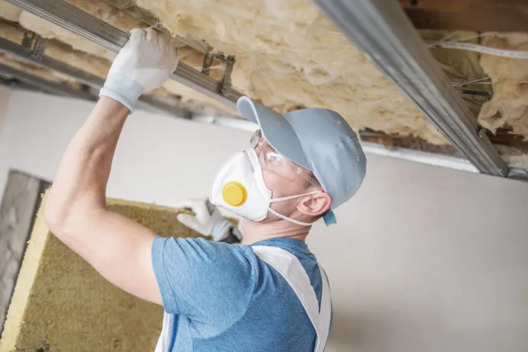Operario con mascarilla colocando lana mineral en el techo durante el trasdosado de una vivienda, quitar humedades Zaragoza precio
