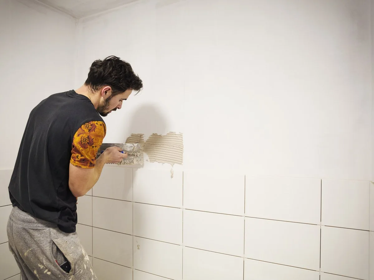 Albañil alicatando con azulejo blanco la pared de un baño, reforma baño por 1000 euros Zaragoza