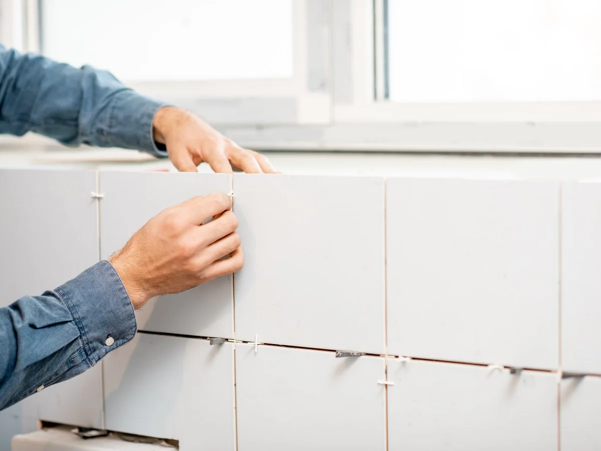 Manos colocando azulejo blanco con crucetas en la pared de un baño, reforma baño por 2000 euros Zaragoza