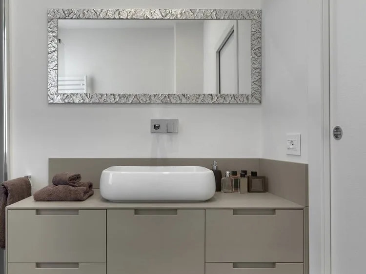 Lavabo blanco sobre encimera gris con mueble de cajones y espejo de marco plateado, reforma baños Zaragoza