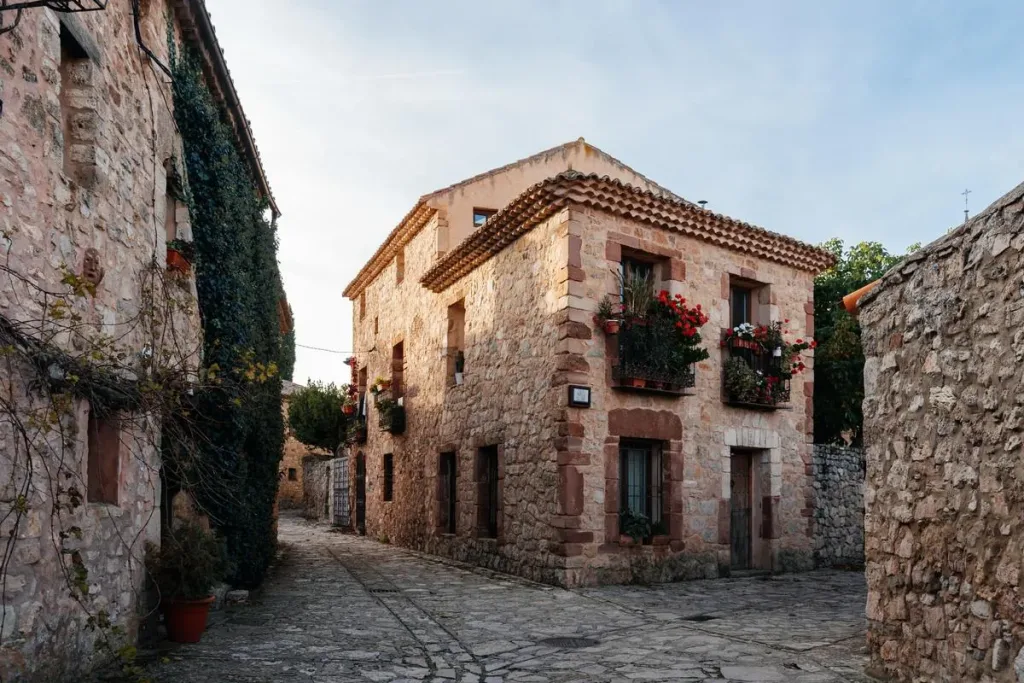 Casa de piedra rehabilitada en una calle empedrada de pueblo, con balcones con flores, reforma de piso o chalet Zaragoza