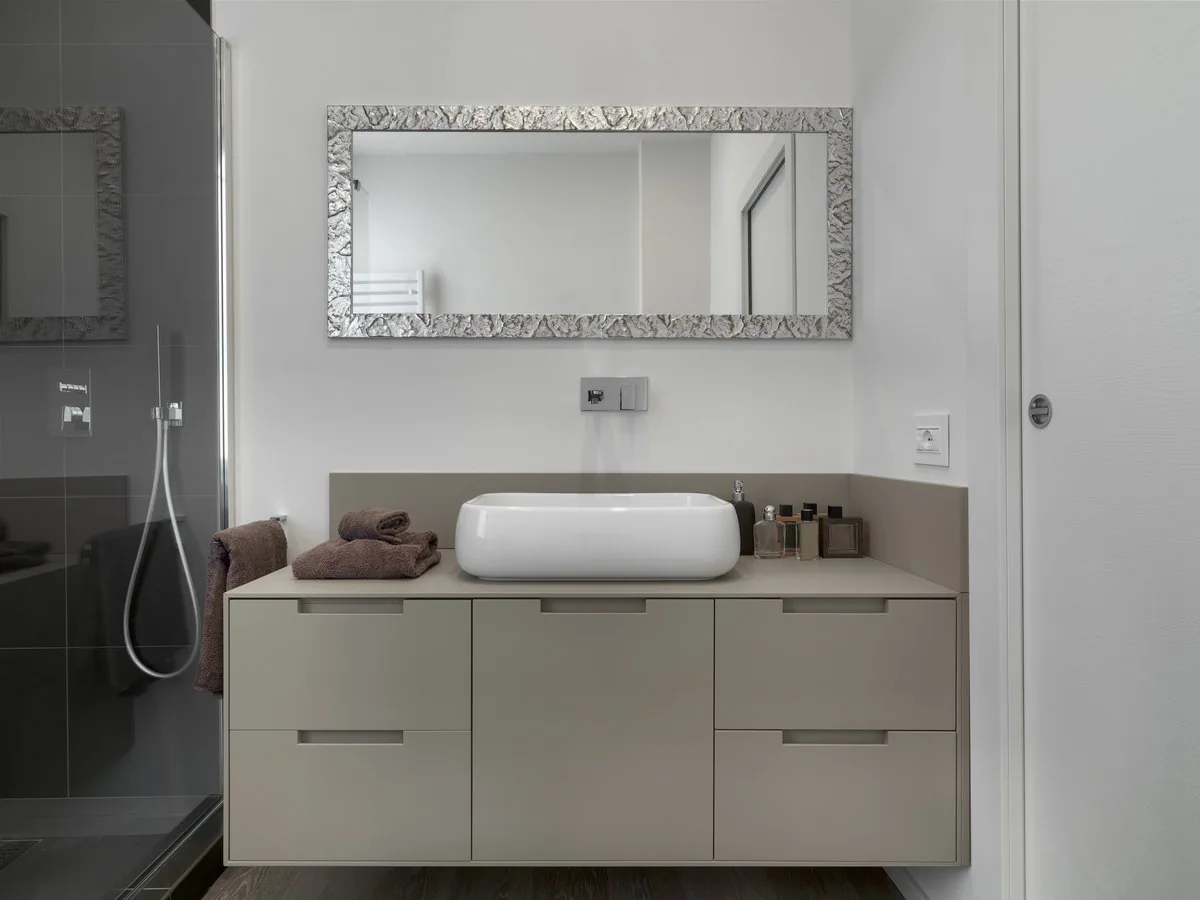 Mueble de lavabo gris con cajones, lavabo sobre encimera, espejo con marco plateado y grifo empotrado, reforma integral de baños en Zaragoza
