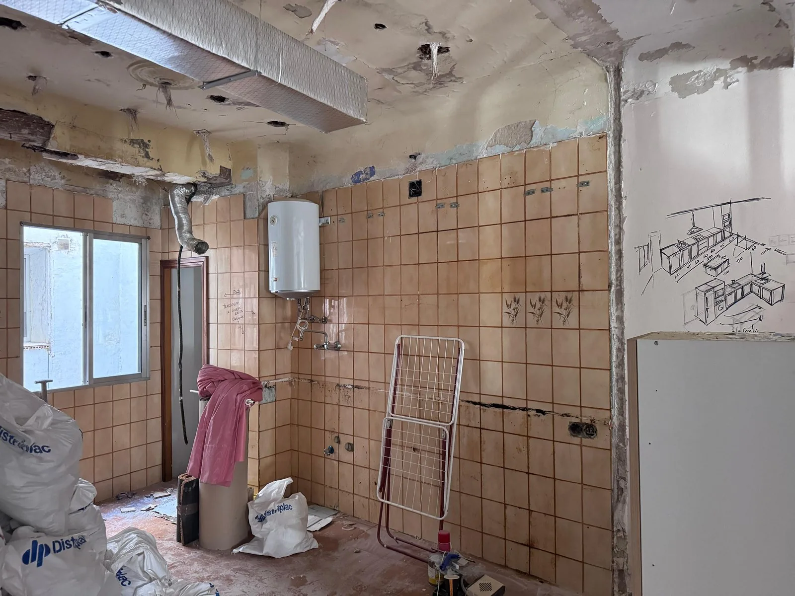Cocina antigua vaciada, con el alicatado viejo a la vista y el boceto de la cocina nueva dibujado en la pared, reforma integral piso antiguo Zaragoza