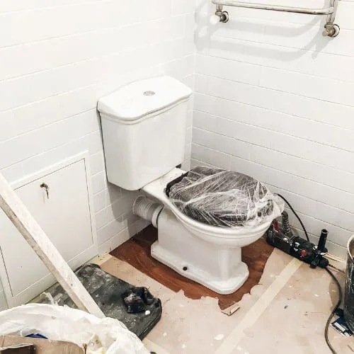 Inodoro tapado con plástico durante la obra, junto a la pared de azulejo blanco y el suelo a medio hacer, reformar baño Zaragoza