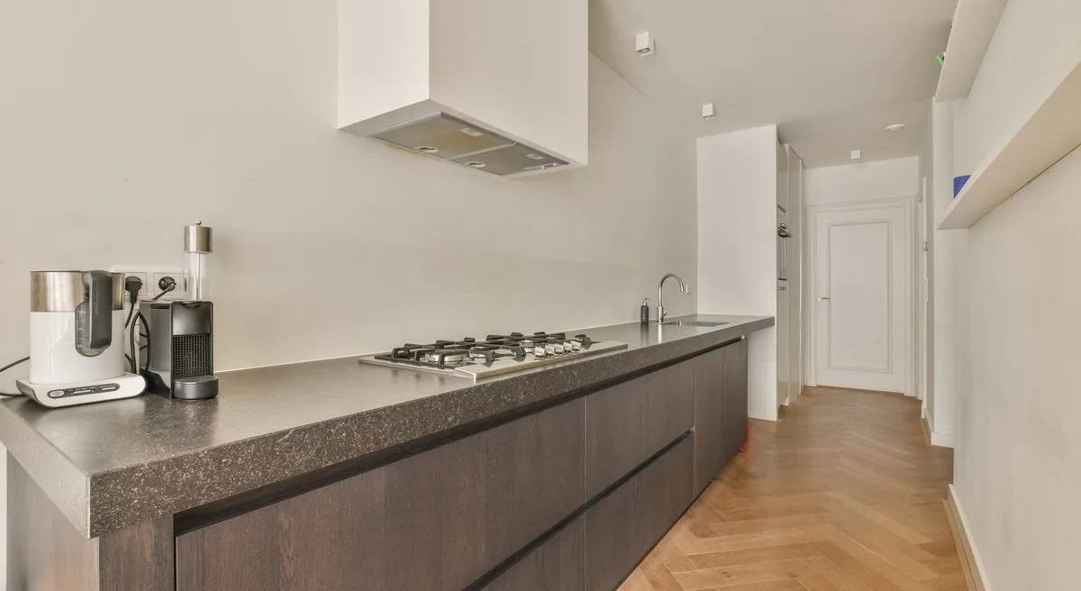 Cocina lineal de un piso reformado con muebles de madera oscura, placa de gas y tarima en espiga, reformar para alquilar Zaragoza