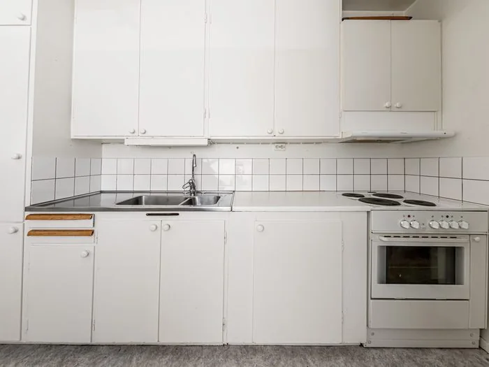 Cocina antigua con muebles blancos, fregadero de acero y placa eléctrica, lista para renovar, reformar una cocina presupuesto Zaragoza